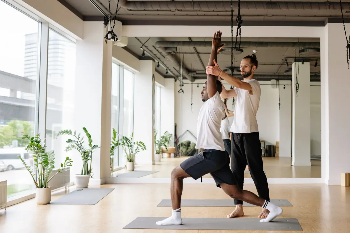 An instructor personally guiding a student through a pose in a bright, plant-filled studio