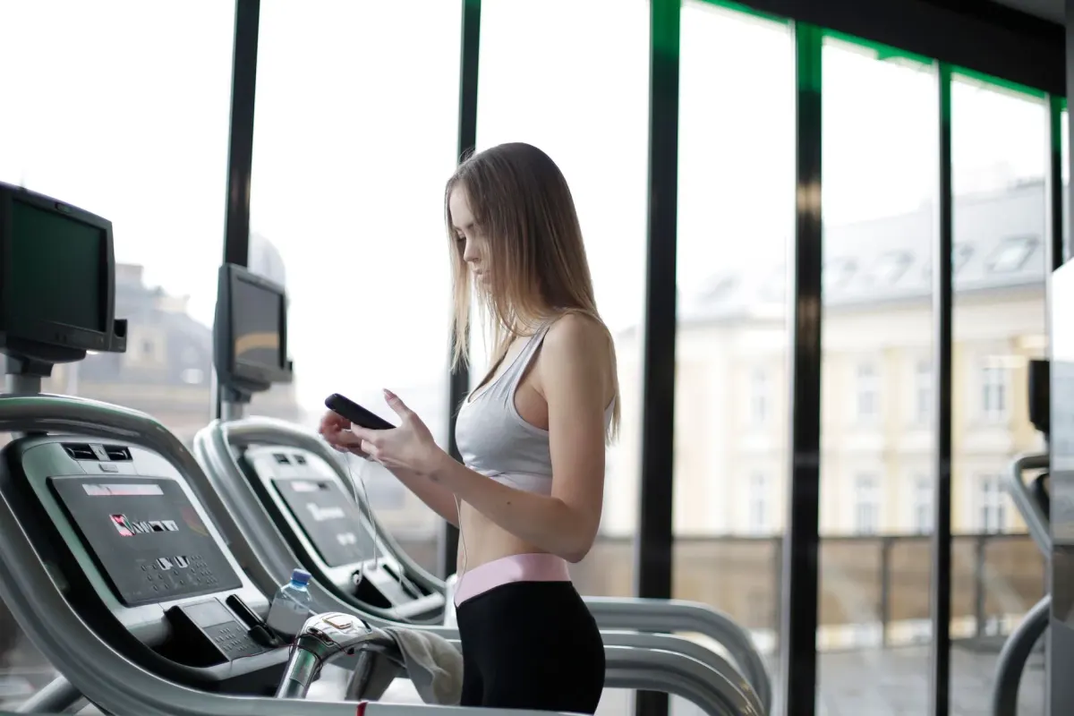A member checking the live class schedule on her phone mid-workout in a modern gym