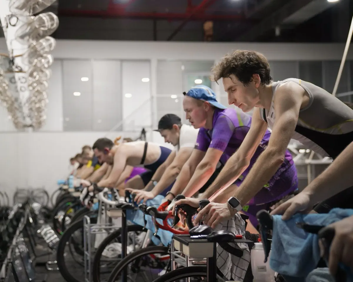 A full row of riders mid-sprint in a dark, high-energy indoor cycling class