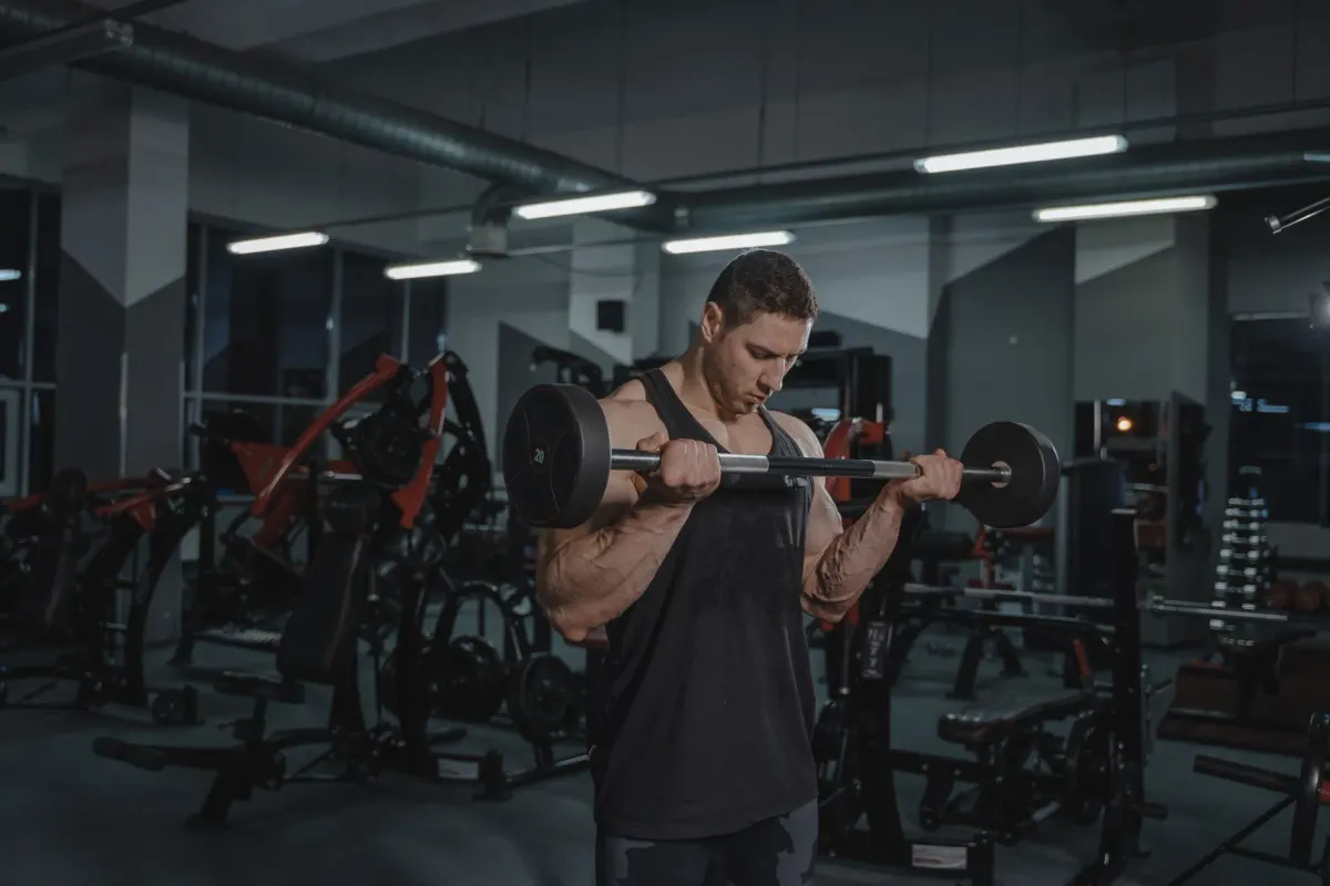 A lifter mid-set on a barbell curl in a moody, fully-equipped strength gym
